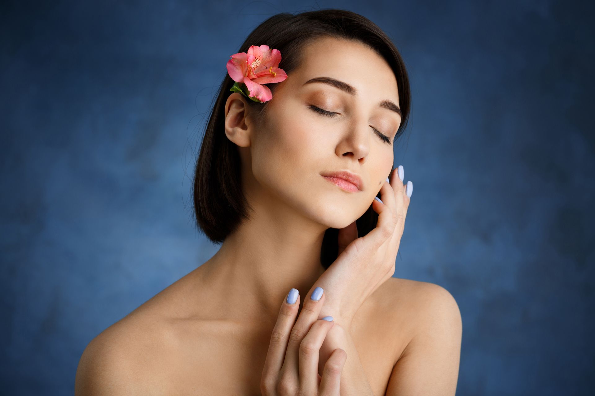 A woman with a flower in her hair is touching her face.