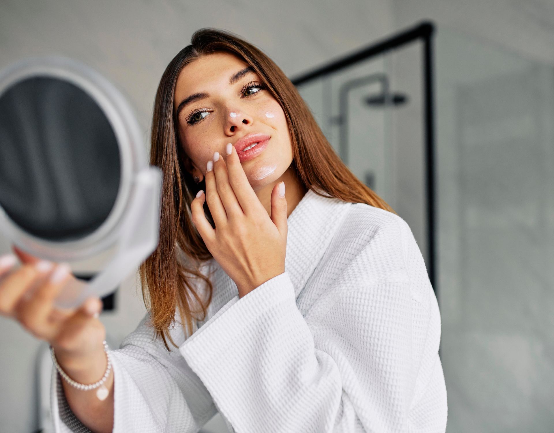 a woman in a bathrobe is looking at her face in a mirror