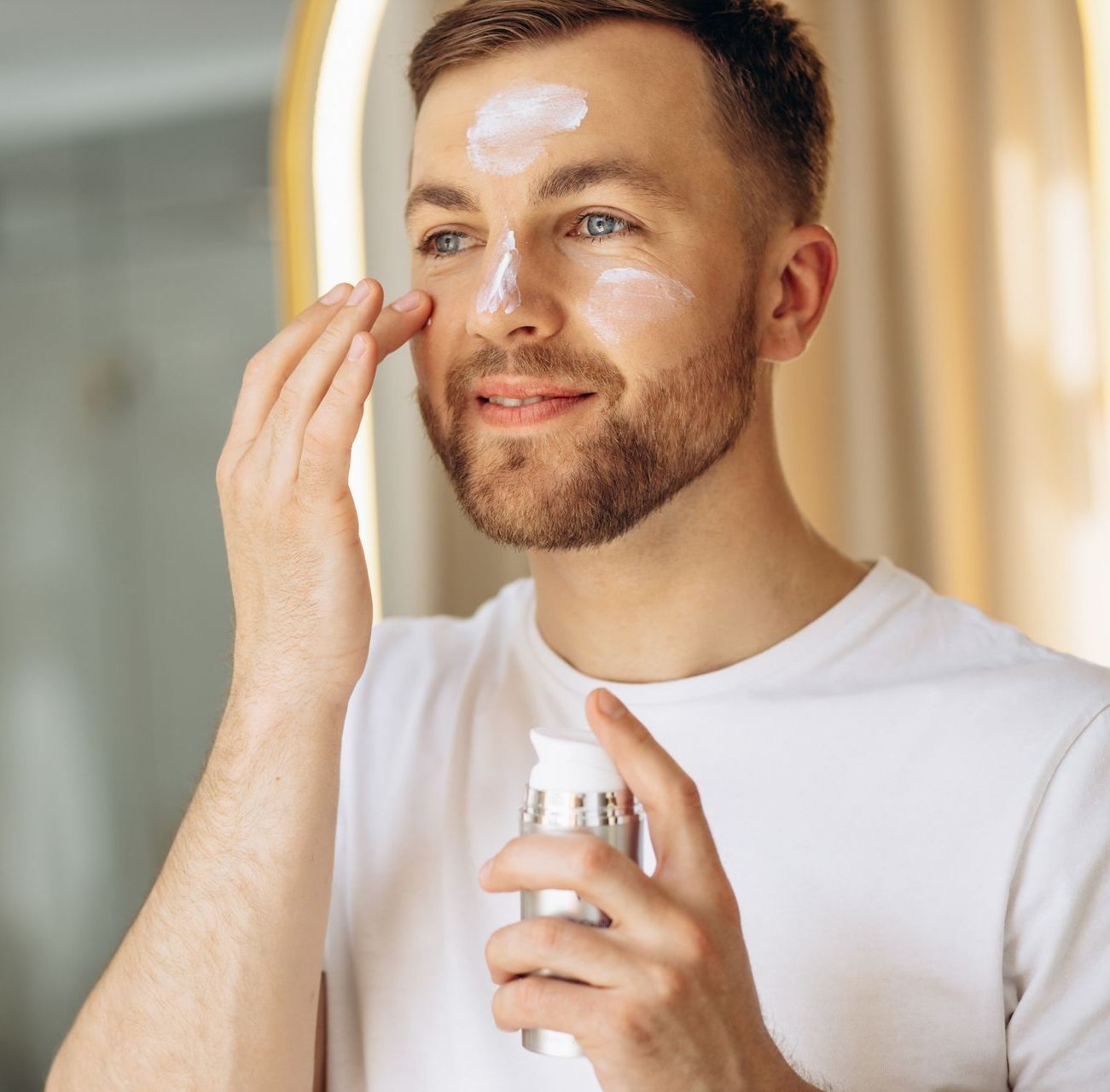 a man in a white shirt is applying lotion to his face