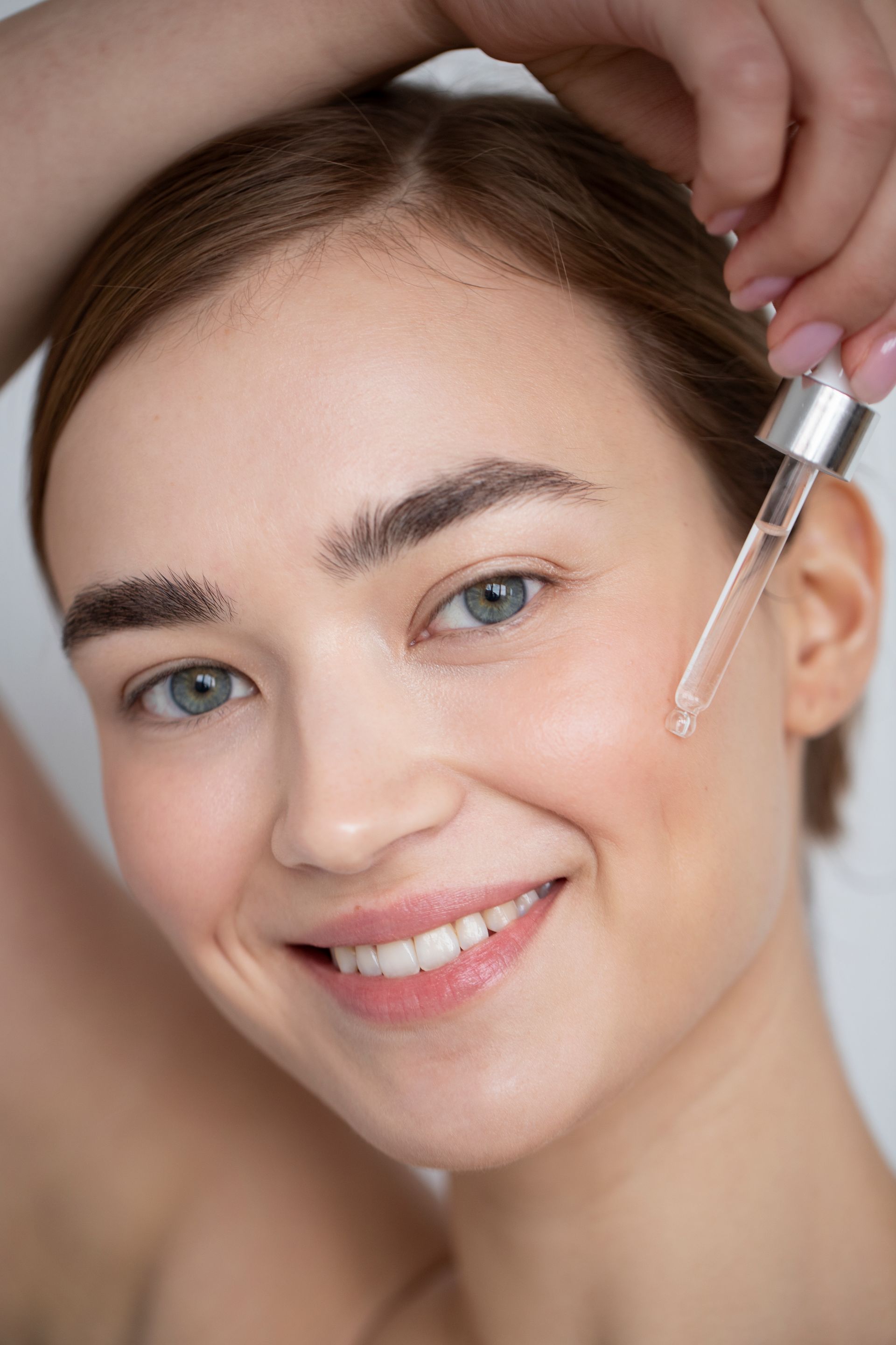 a woman is smiling while applying a serum to her face
