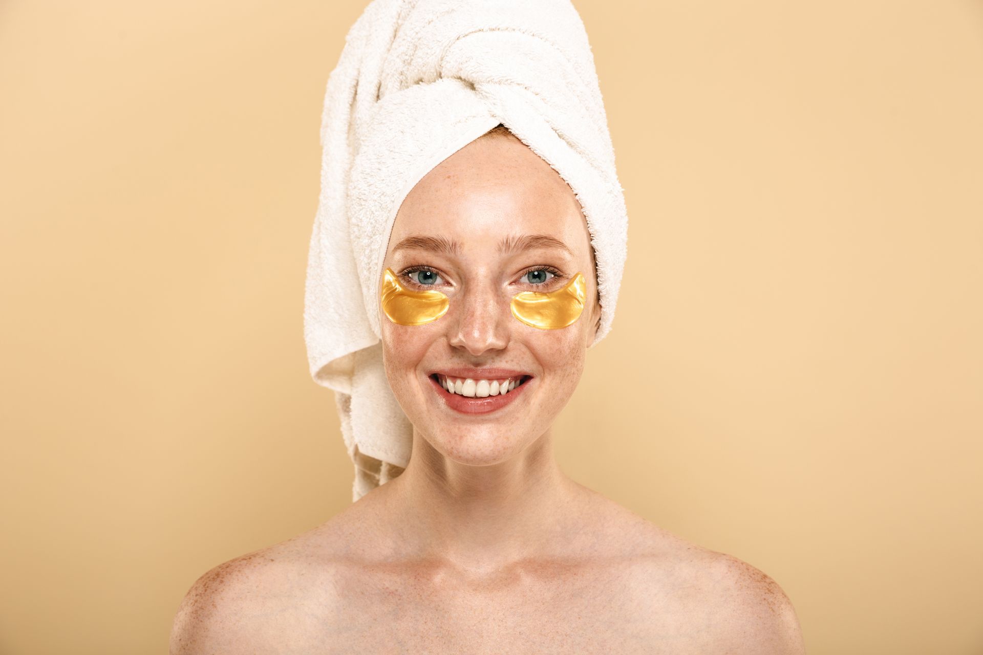 a woman with a towel wrapped around her head has gold eye patches on her face