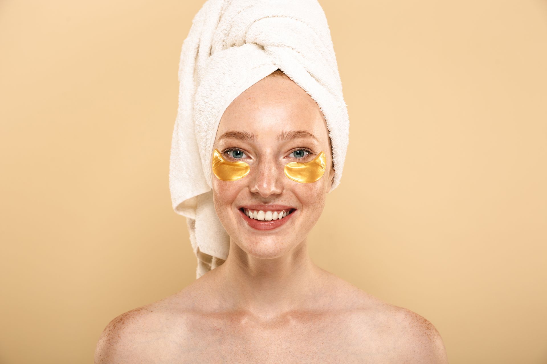 A woman with a towel wrapped around her head and gold eye masks on her face.