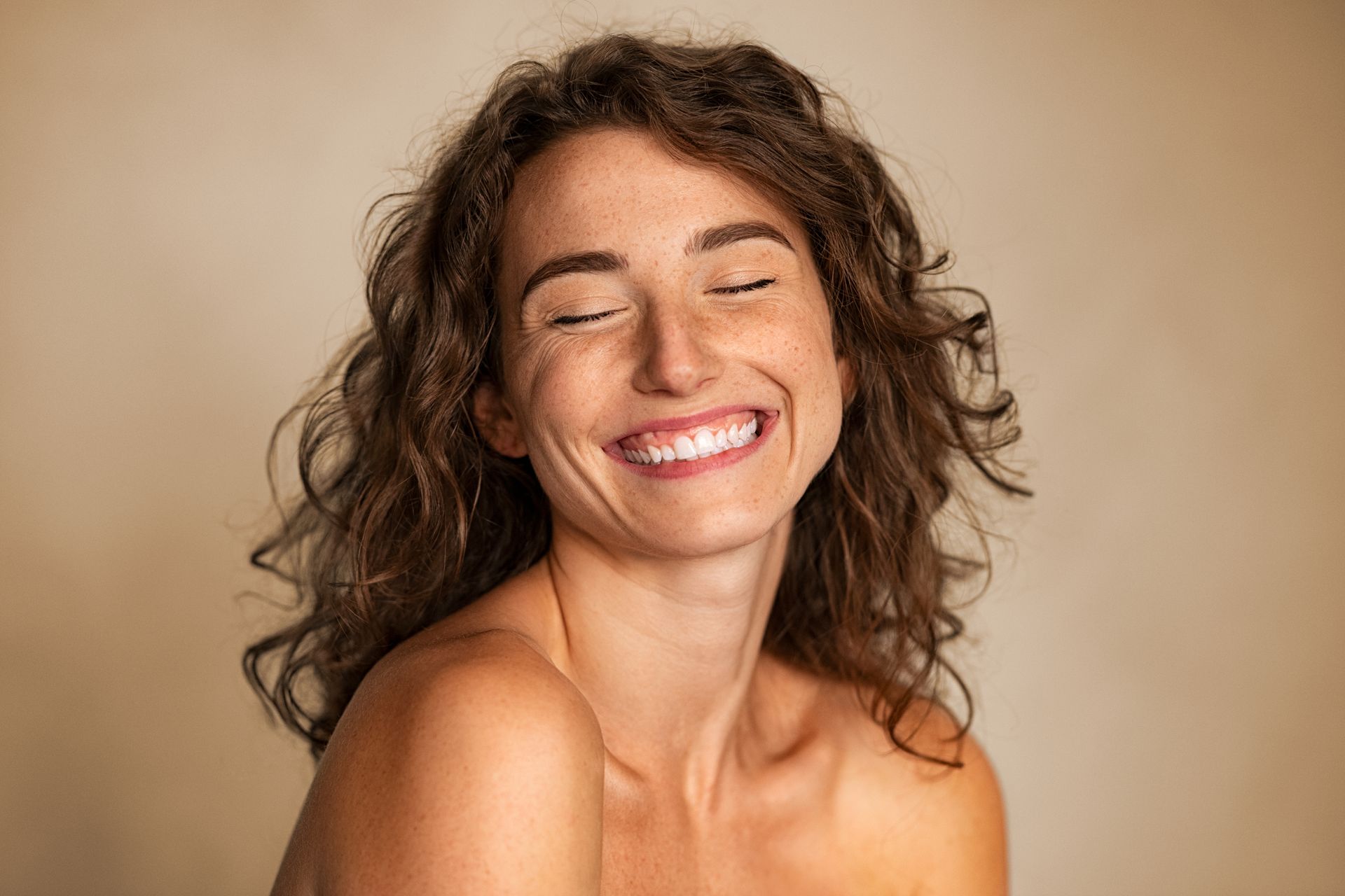 A woman with curly hair is smiling with her eyes closed.