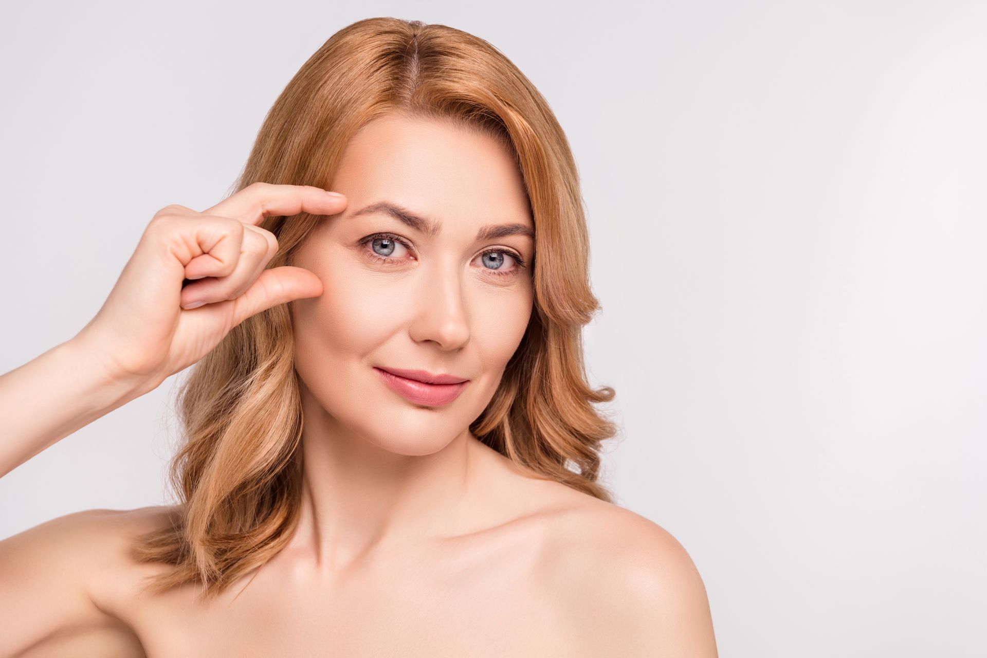 A woman is pointing at her eyebrow with her finger.