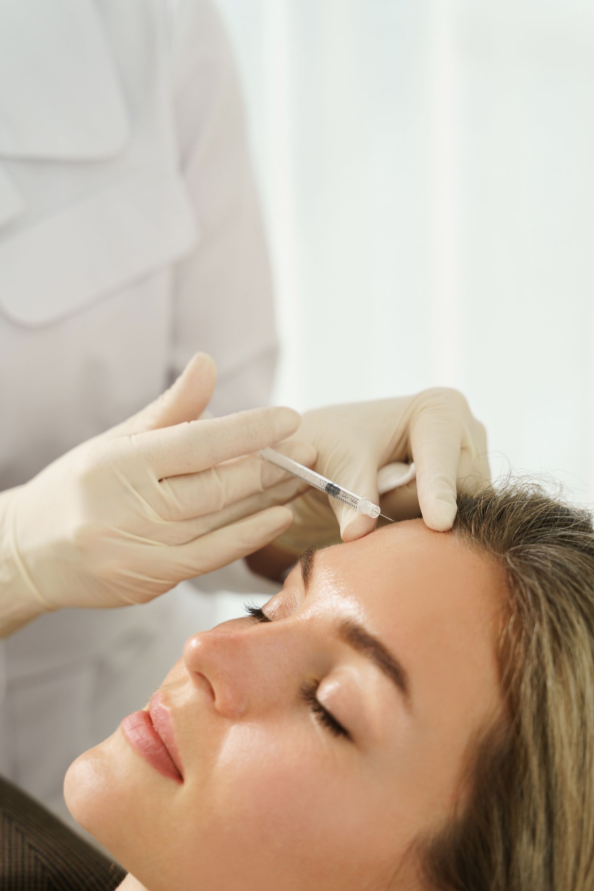 A woman is getting a botox injection in her forehead.