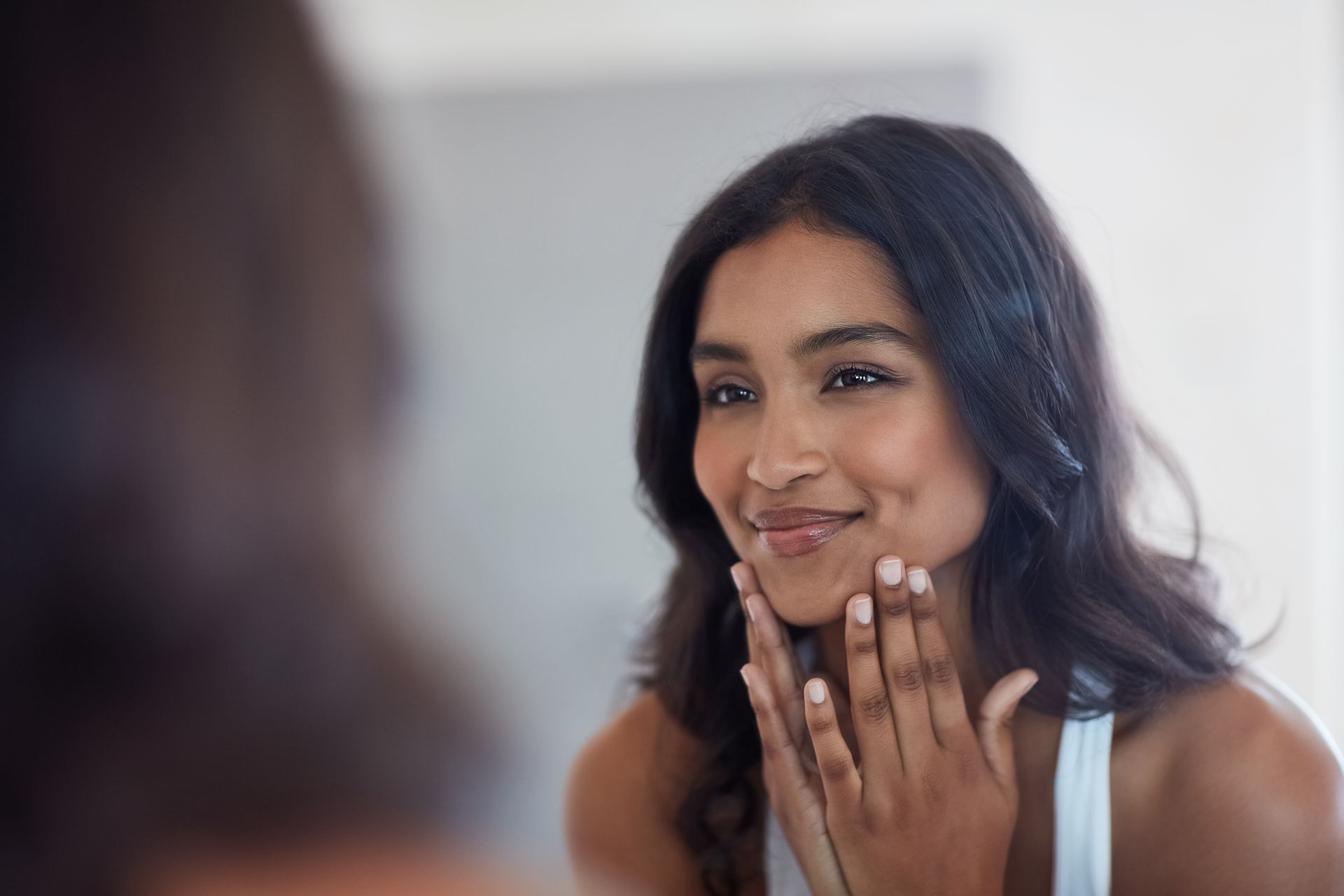 A woman is looking at her face in the mirror and smiling.