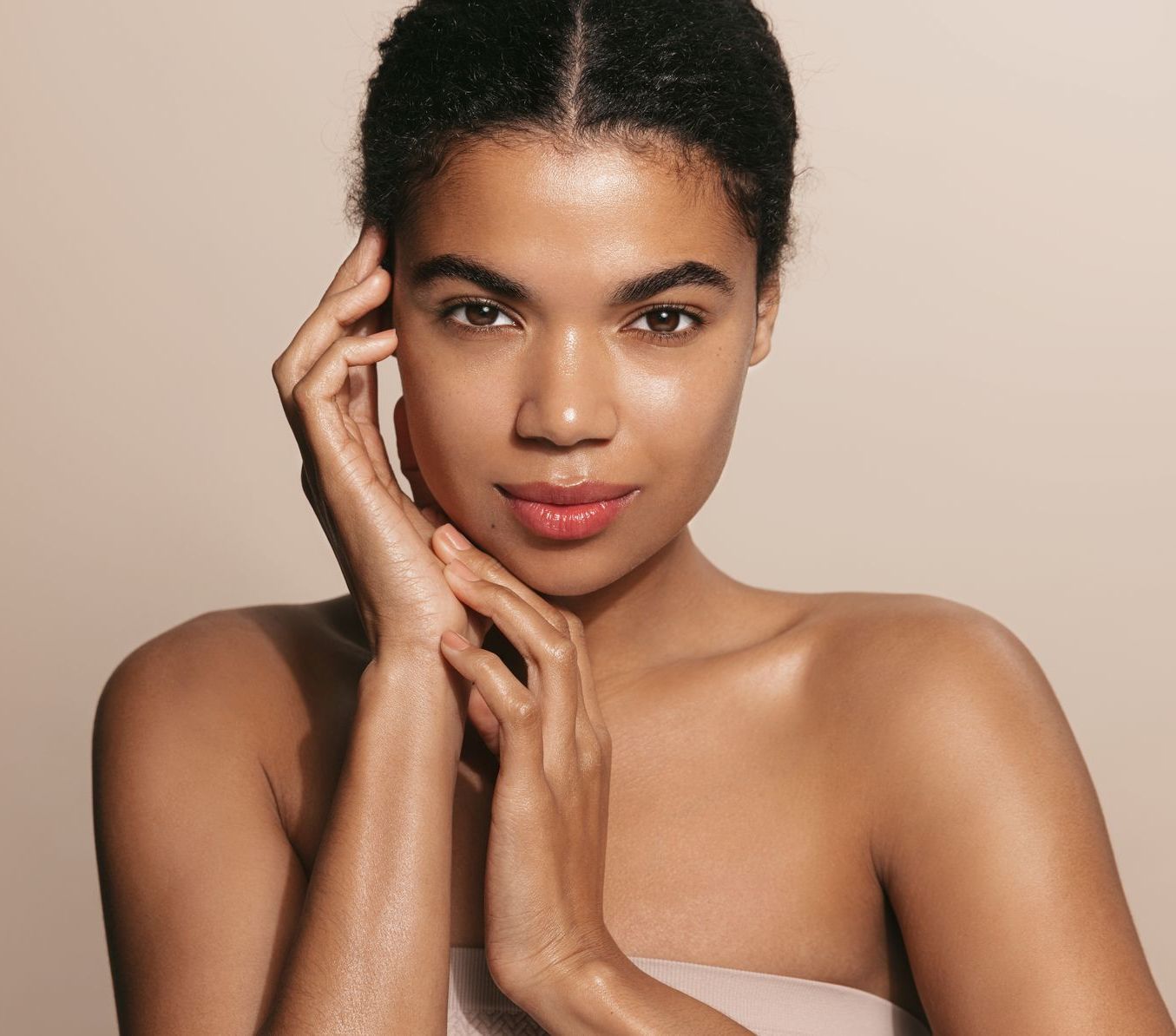 A woman with her hands on her face is looking at the camera.