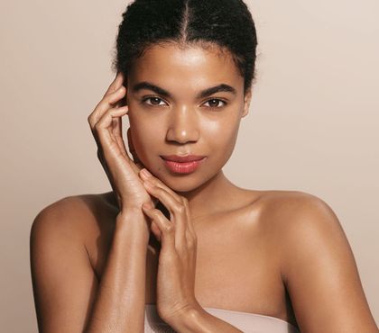 A woman with her hands on her face is looking at the camera.