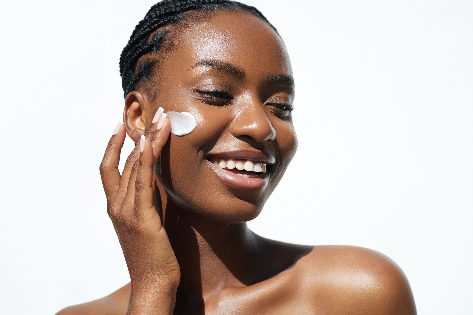 A woman is smiling while applying cream to her face.