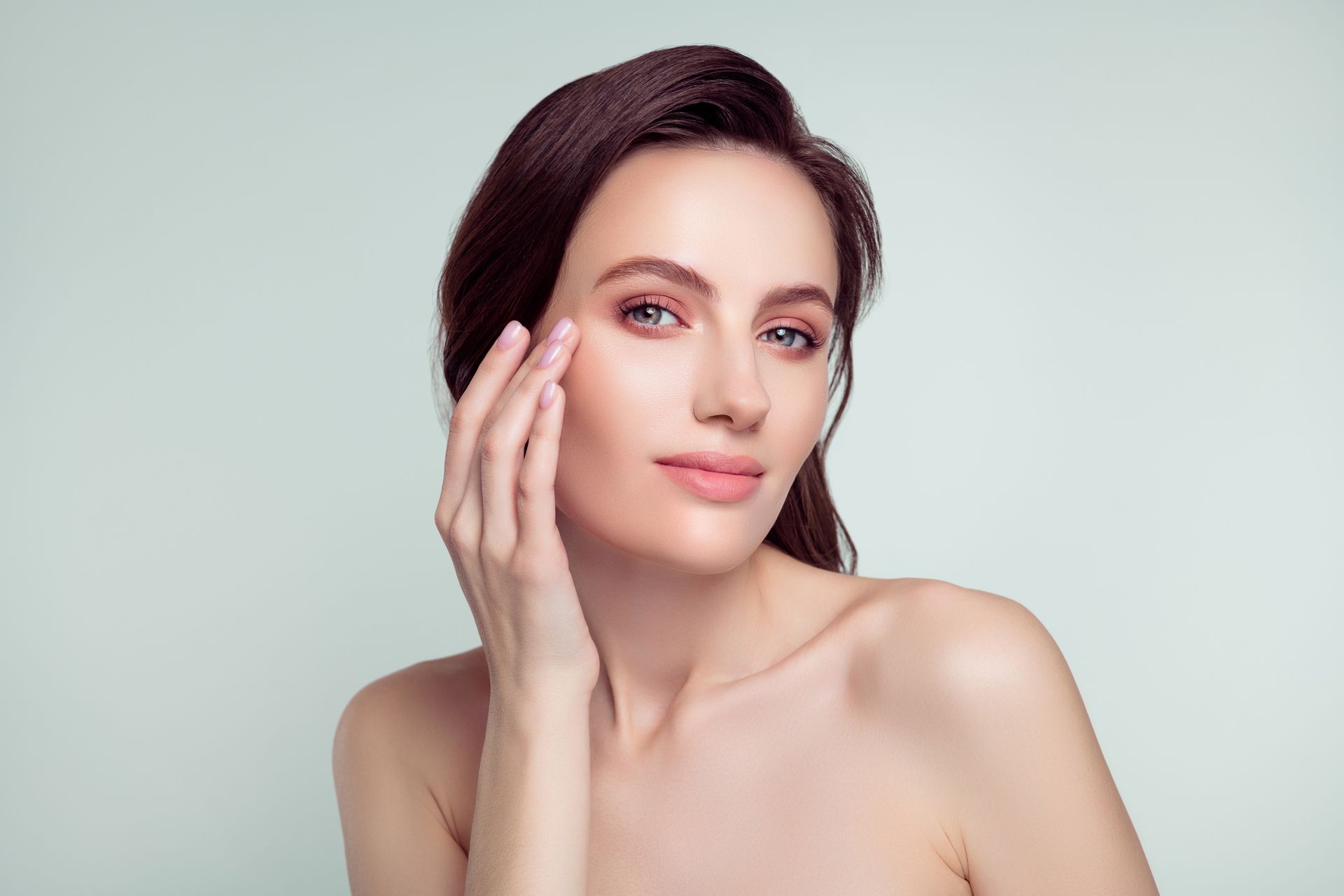 A woman is touching her face with her hand and looking at the camera.