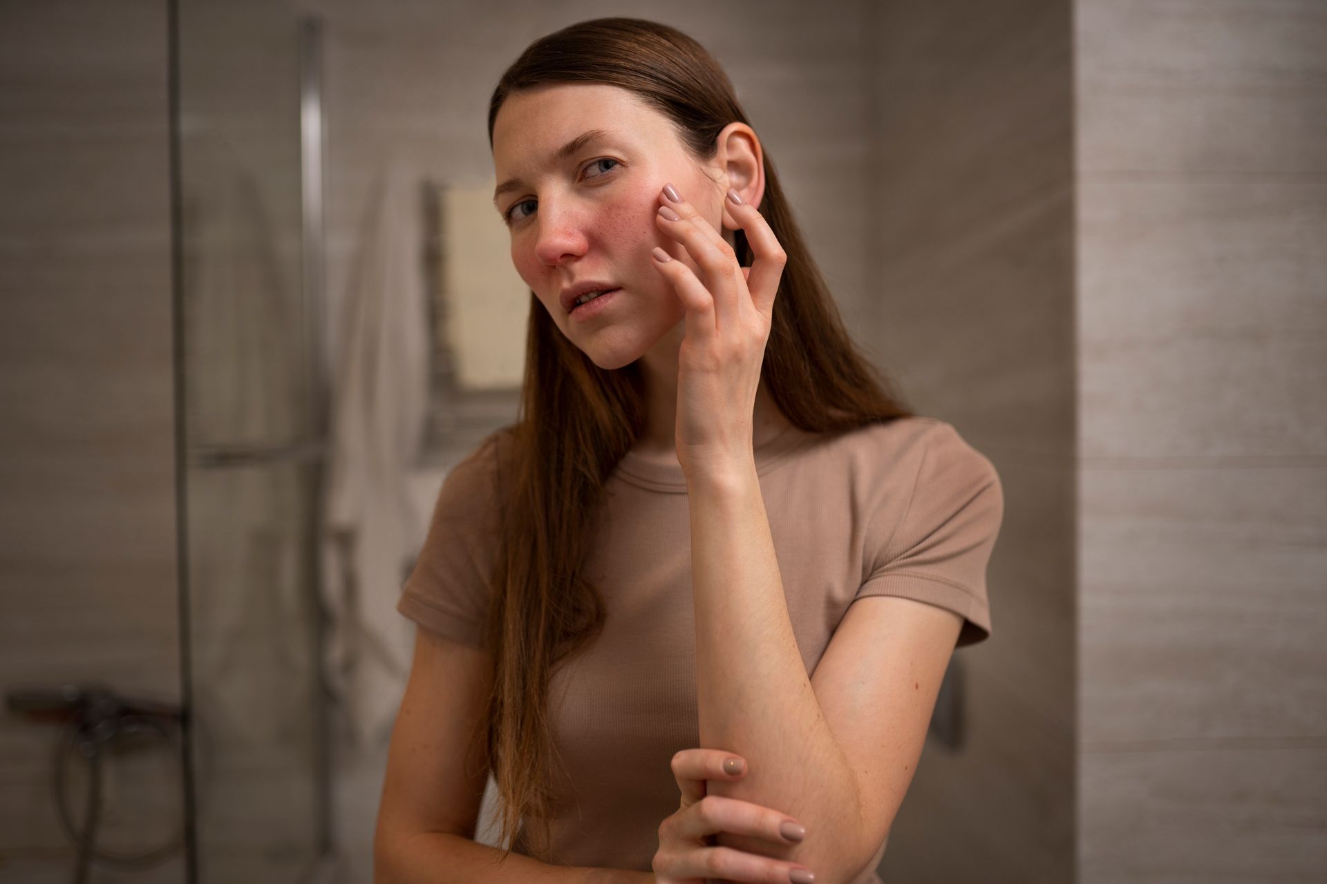 A woman is looking at her face in the mirror in a bathroom.