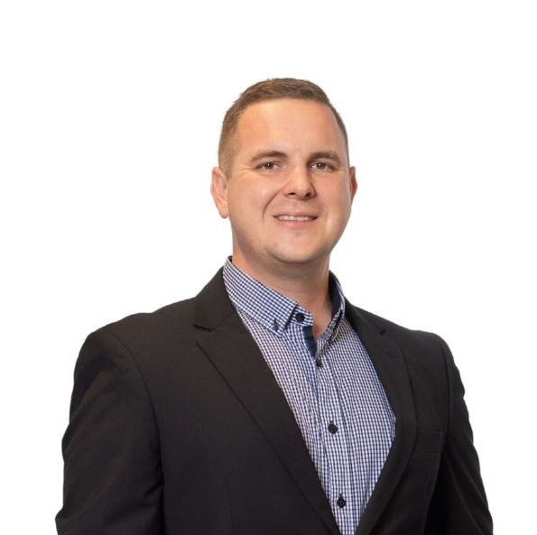 Juan Crafford in a black suit jacket and checkered blue shirt, smiling.