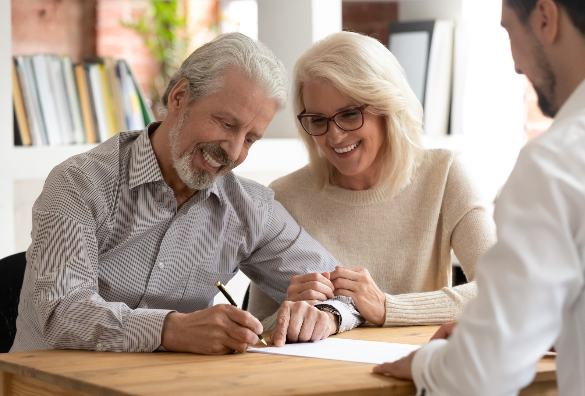 An elderly couple is signing a document with a man.