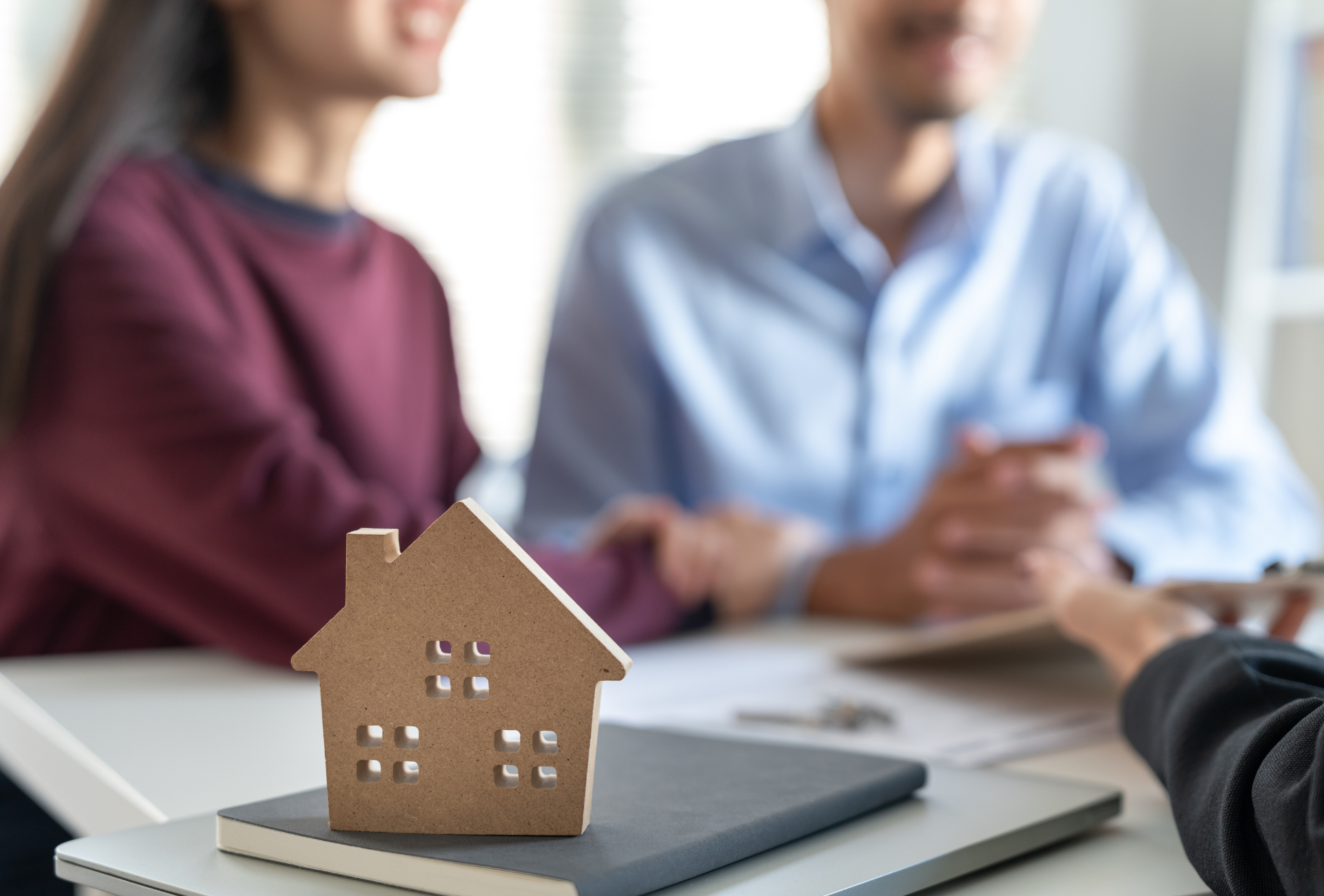 A couple is sitting at a table with a model house on top of a book.