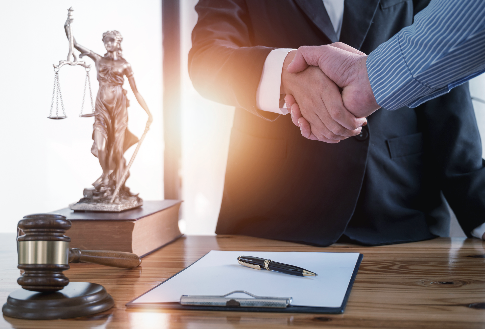 Two men are shaking hands in front of a statue of justice.