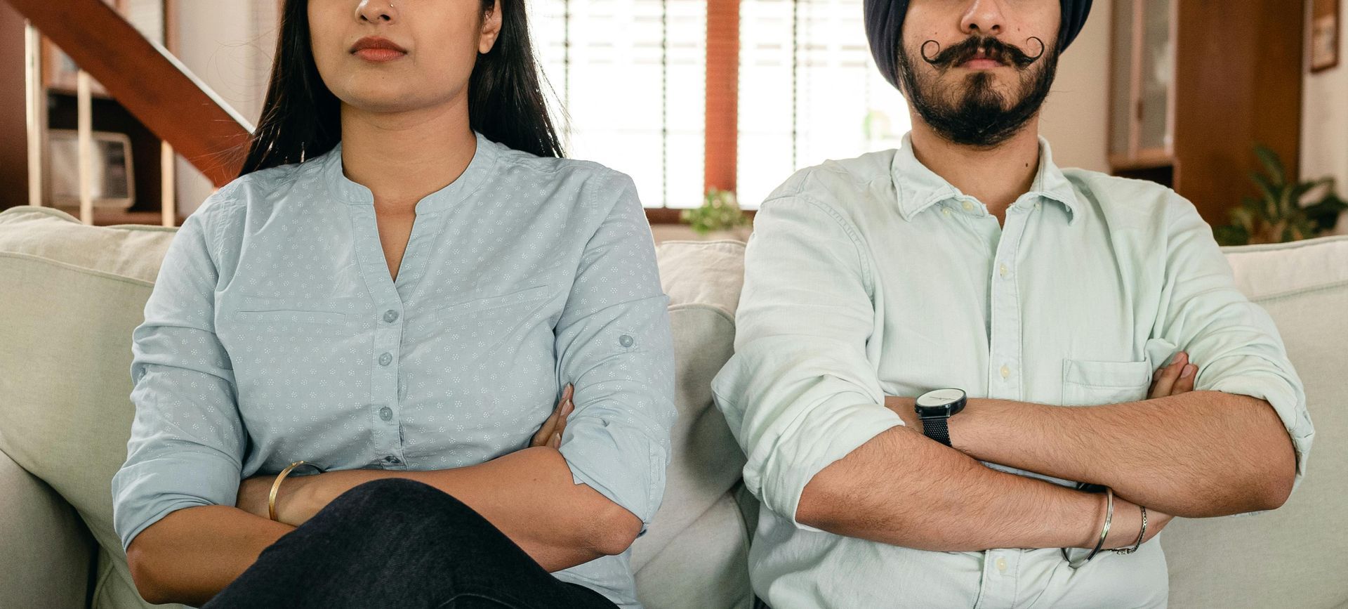 A man and a woman are sitting on a couch with their arms crossed.