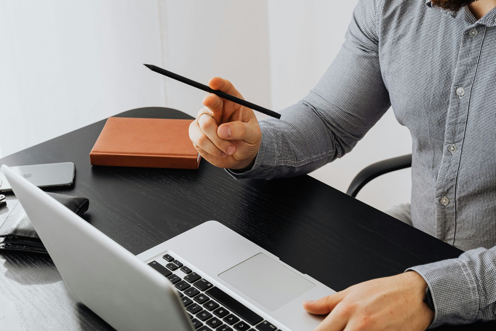 A man is sitting at a desk using a laptop computer and holding a pen.