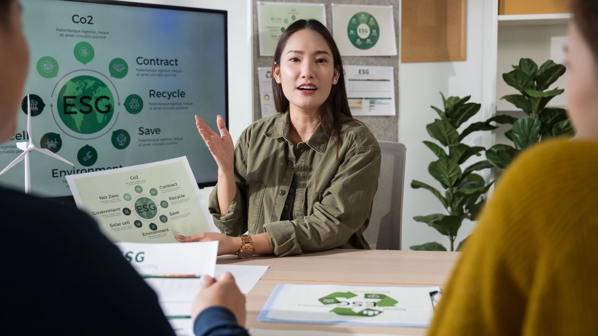Woman presenting ESG plan in a meeting, pointing to charts with environment-themed graphics.