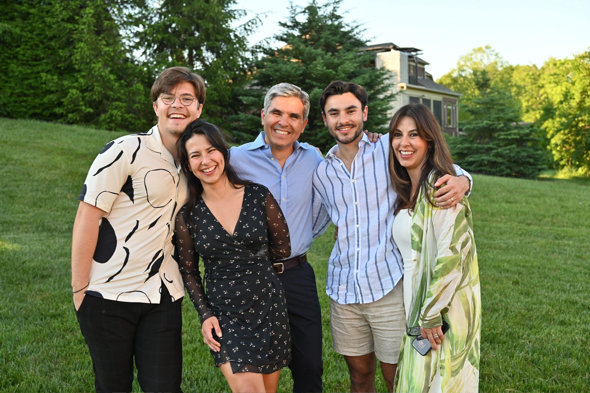 Family poses together outdoors on a grassy lawn; two women, three men, smiling.