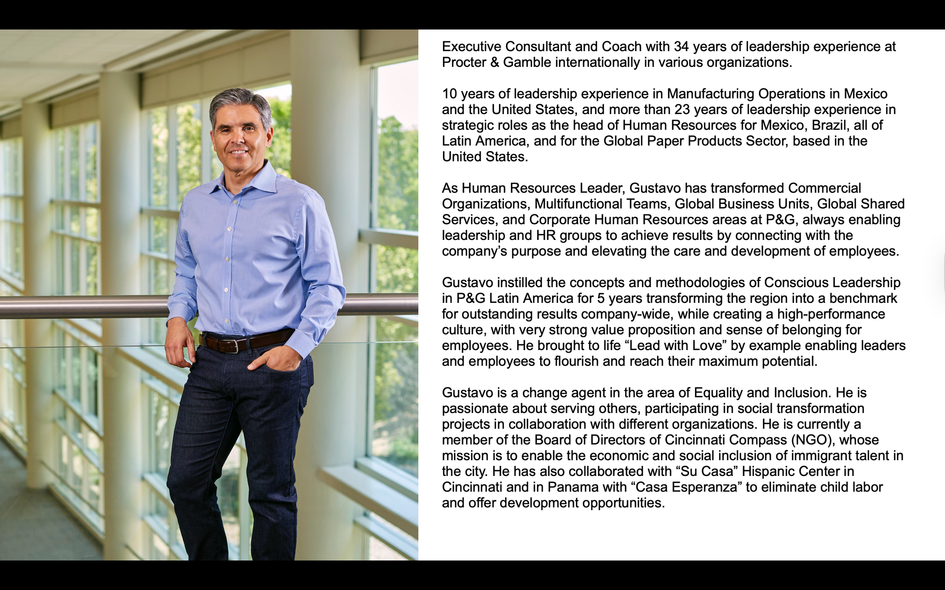 Man in button-down shirt and jeans stands by a window in a bright hallway, smiling, with text description alongside.