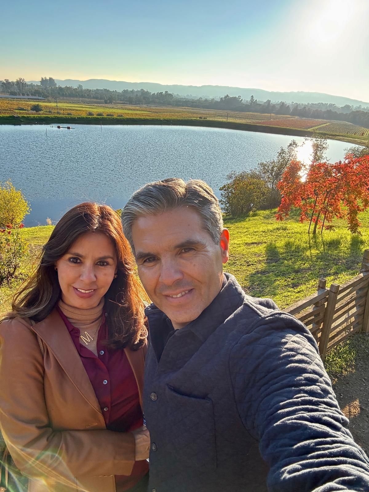 Couple taking a selfie with a lake and fall foliage in the background. Sunny day.