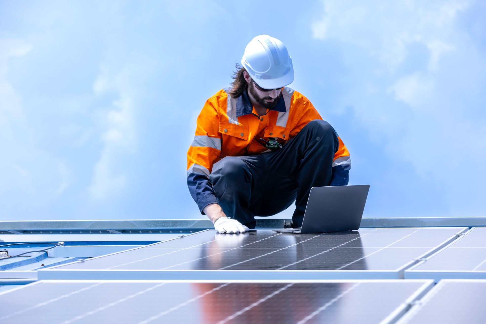 View of a solar panel technician with safety gear checking a panel against blue sky.