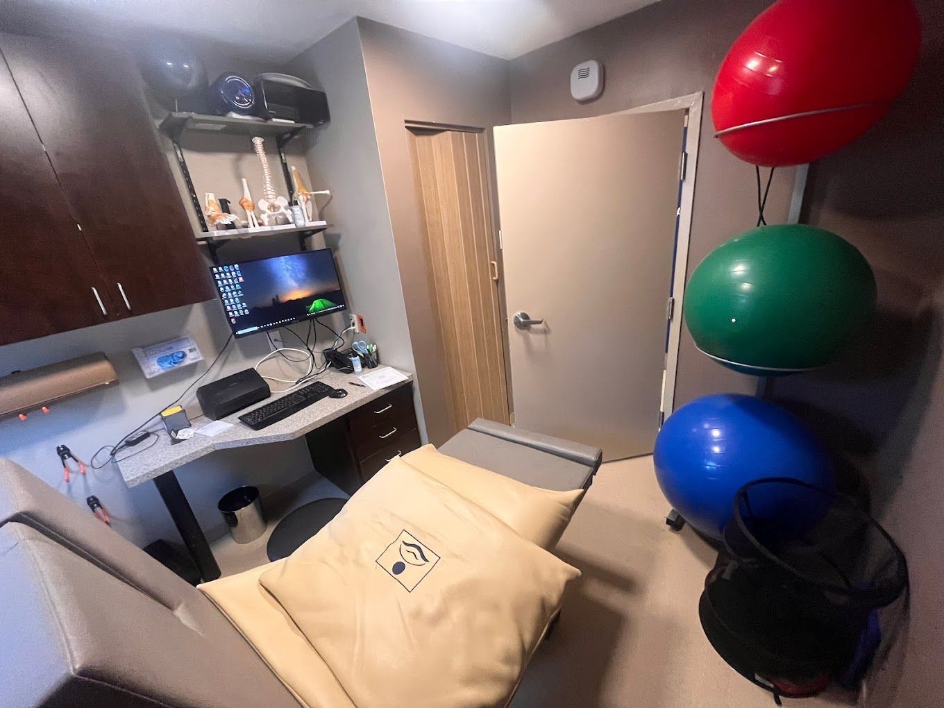 A room with a chair , desk , computer and exercise balls