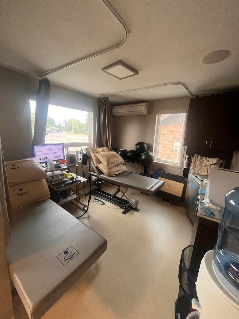 A room with a bed , desk , computer and water cooler.