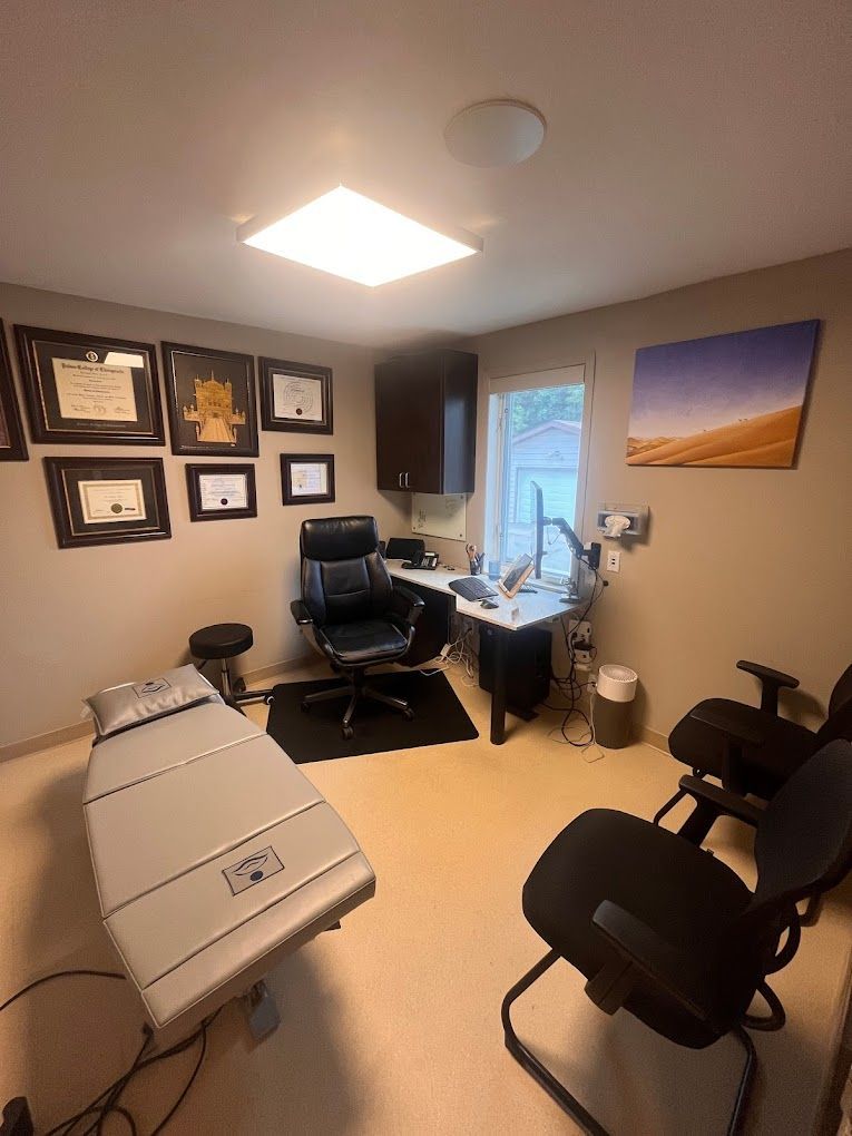 A doctor 's office with a bed , chair , desk and a window.