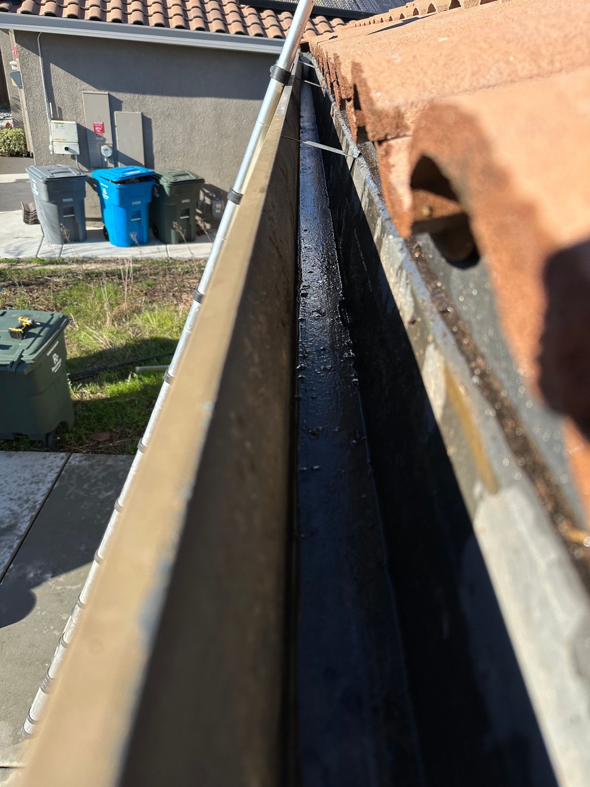 A gutter with water coming out of it and a roof in the background