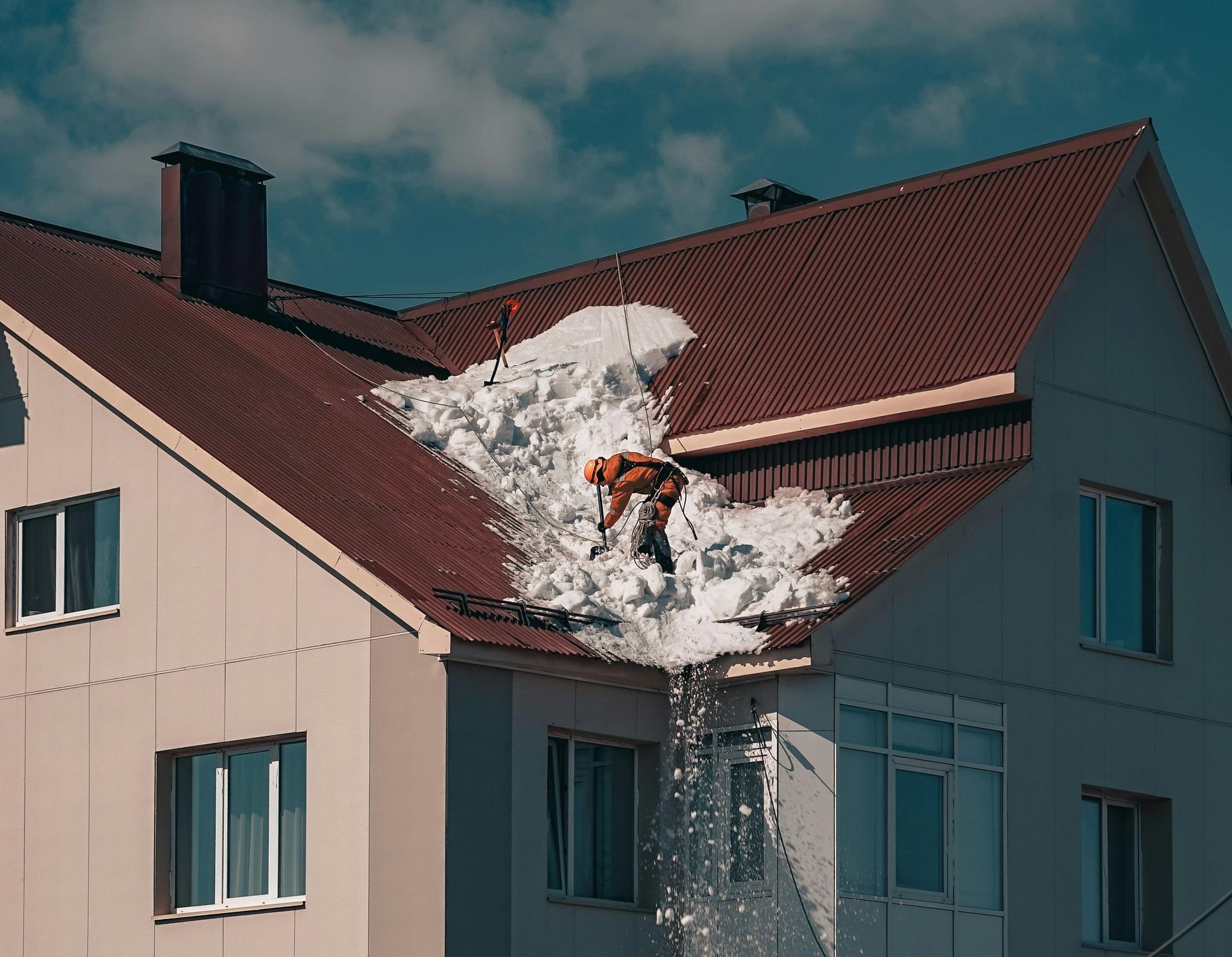 A man is clearing snow from the roof of a house.