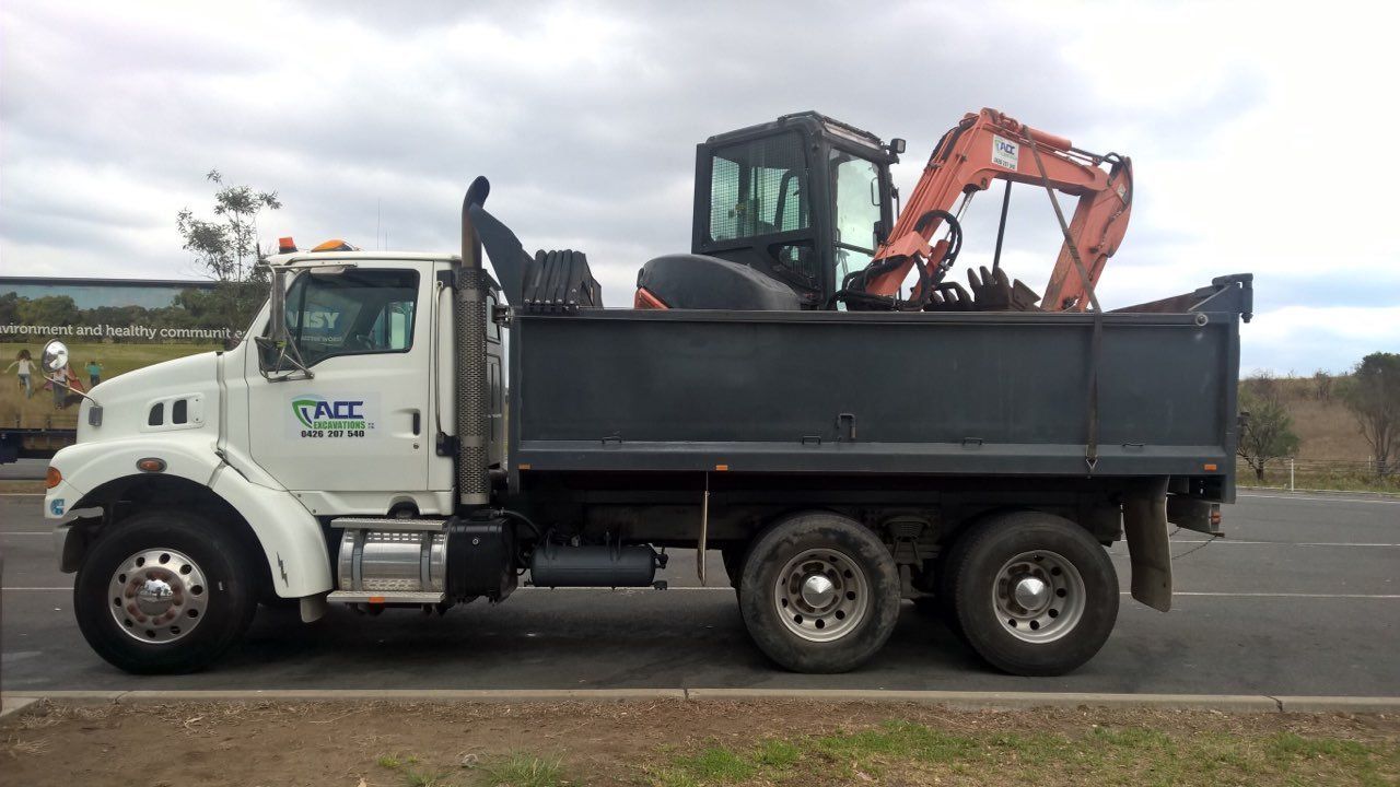 A Dump Truck With An Excavator In The Back Is Parked — ACC Excavations & Demolition Pty Ltd In Nowra, NSW