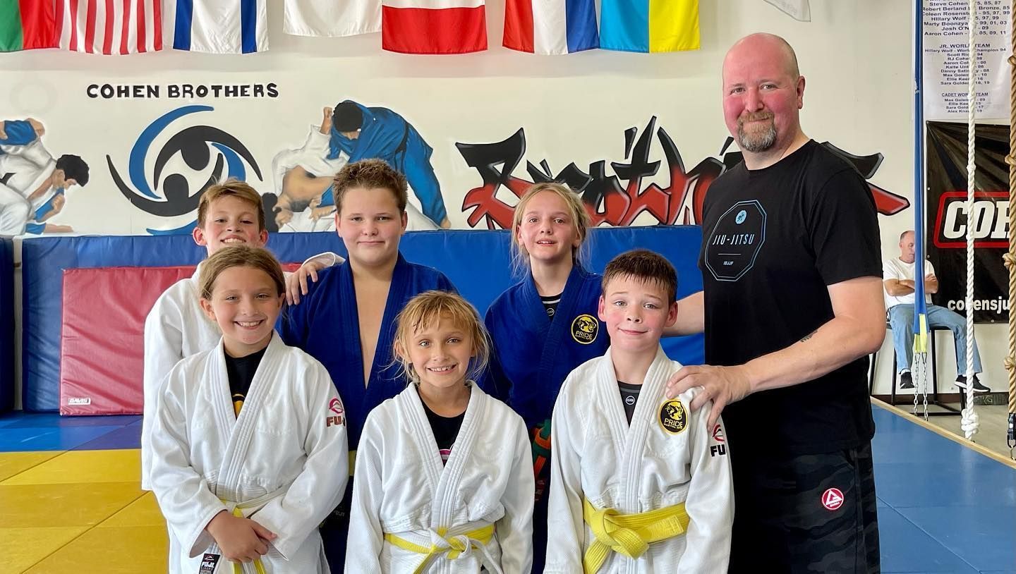 Group of children in martial arts attire posing, some with arms around each other, in a gym.