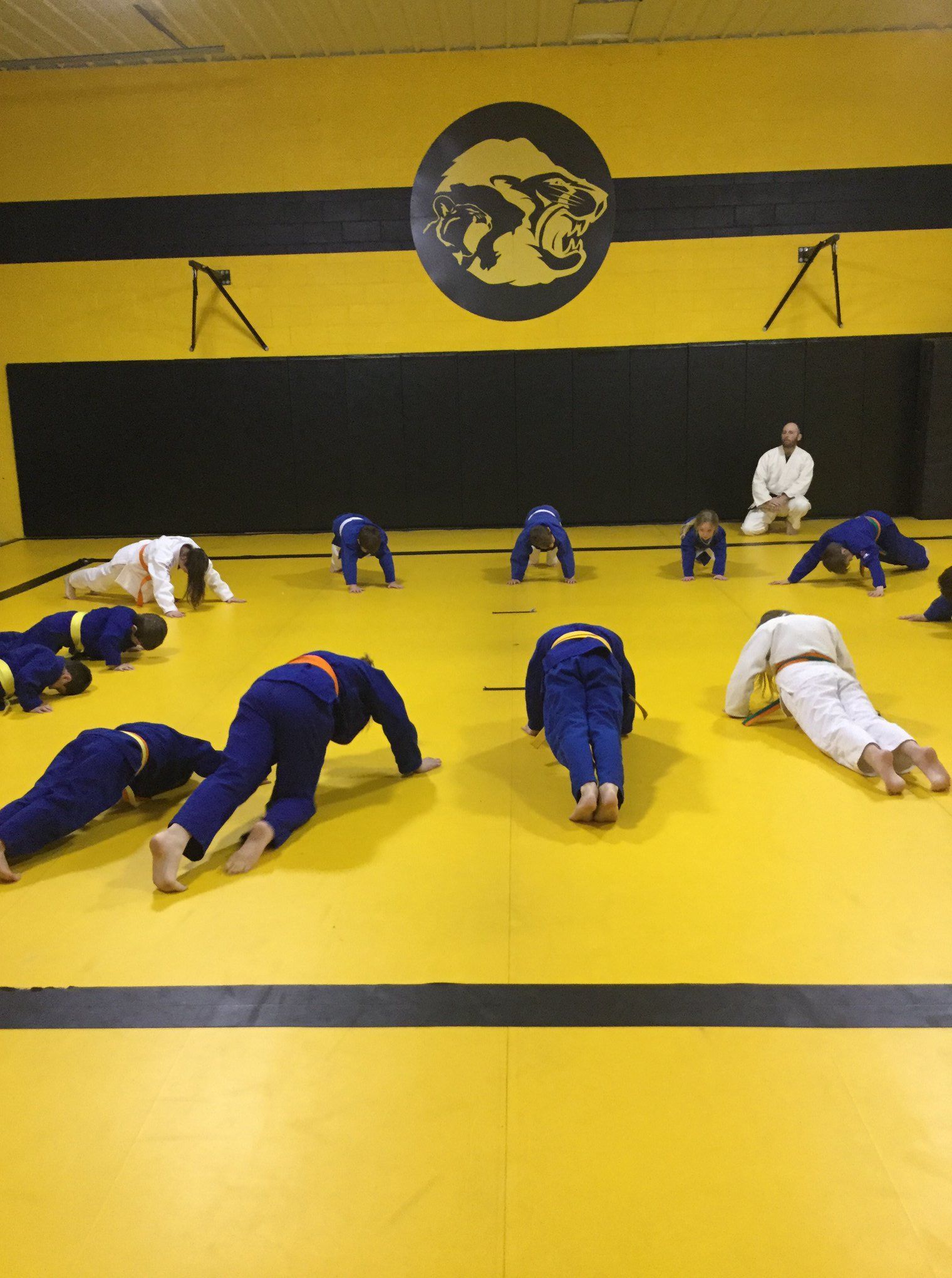Five people in jiu-jitsu gear pose together in a gym.  Smiling,  some have arms around each other. Machado logo visible.