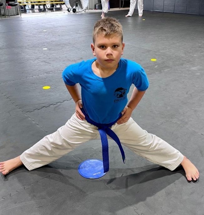 Two people grappling on a mat, one in a black gi, the other in a rash guard, legs entangled.