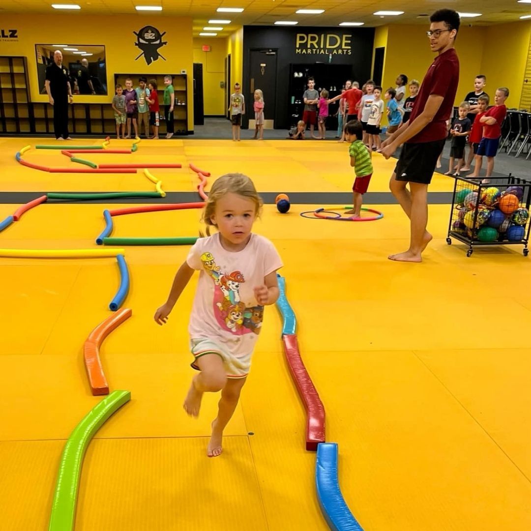 Two boys on a mat practicing Jiu-Jitsu. One boy is on top, giving a thumbs-up.