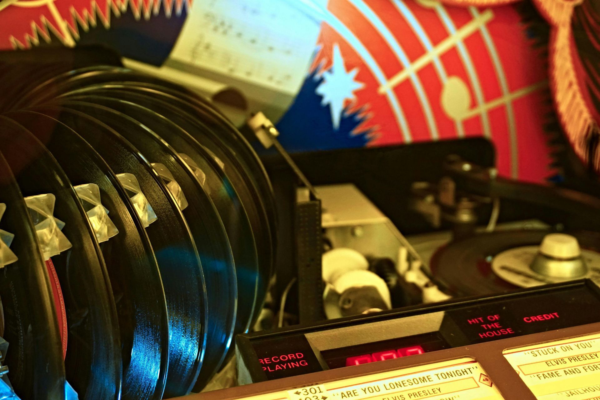 Jukebox holding stacks of vinyl records with a red digital display, in a dimly lit interior.