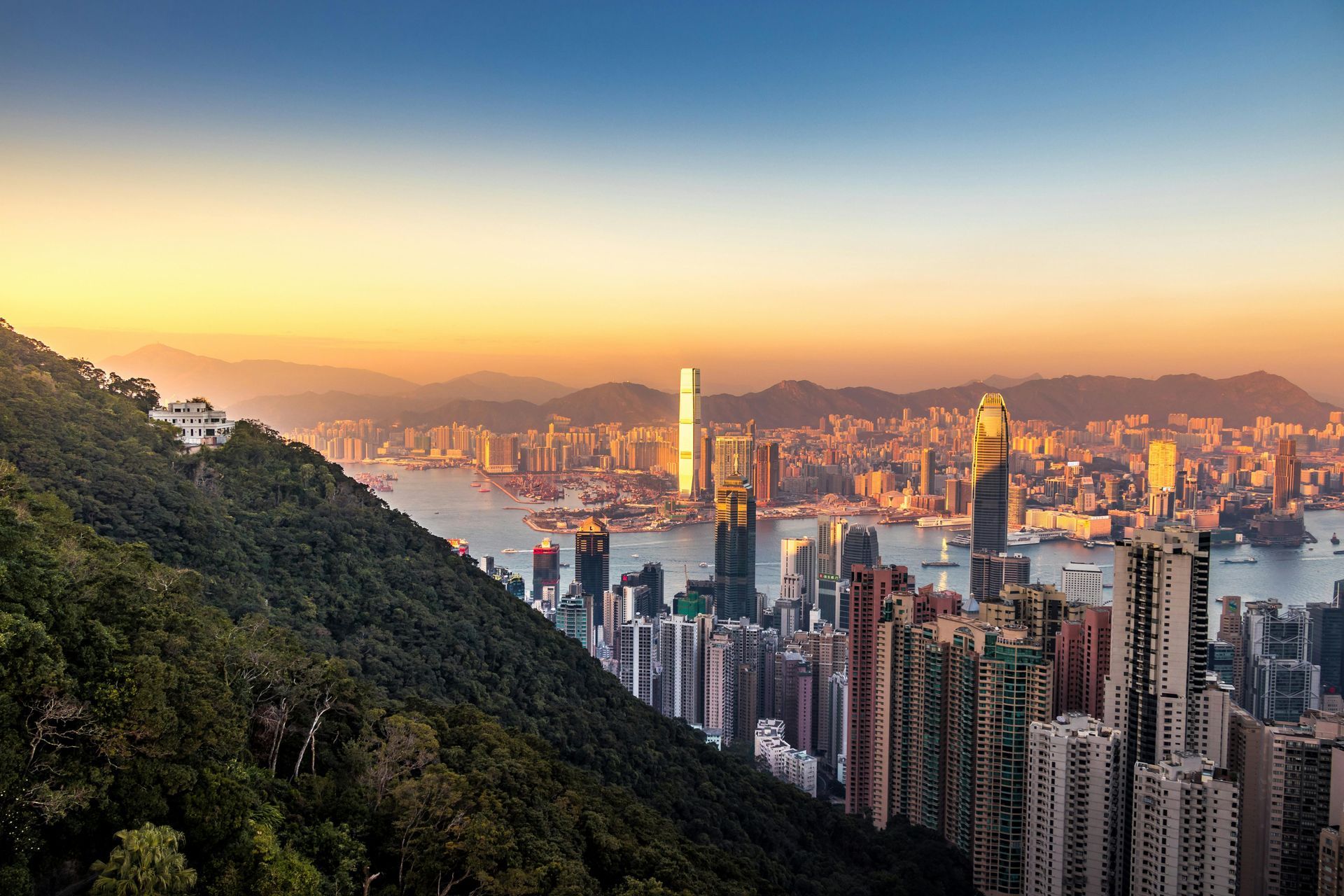 Cityscape of Hong Kong with skyscrapers and harbor at sunset.
