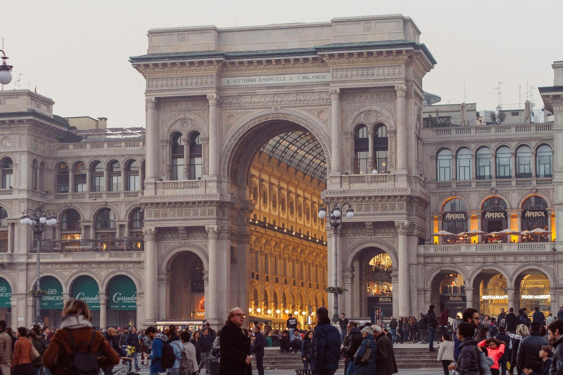 Arched entrance to the Galleria Vittorio Emanuele II in Milan, Italy, with crowds of people gathered.