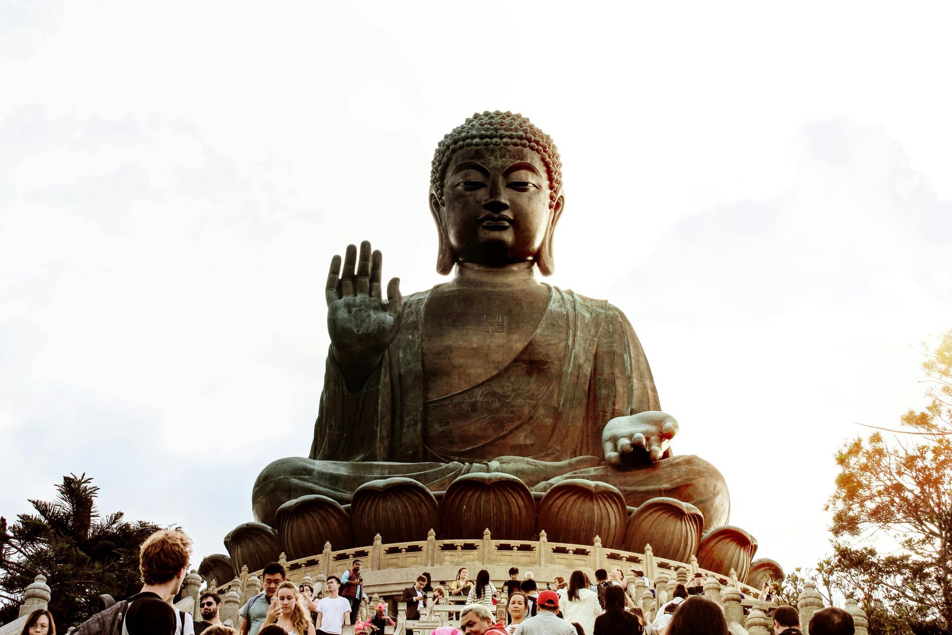 Giant bronze Tian Tan Buddha statue in Hong Kong, hand raised in blessing, people gathered below.