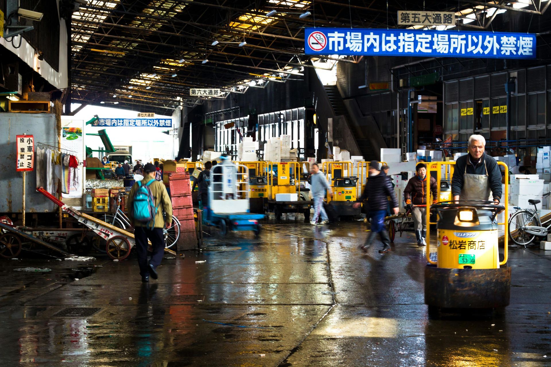 Busy fish market with forklifts, workers, and a wet floor.