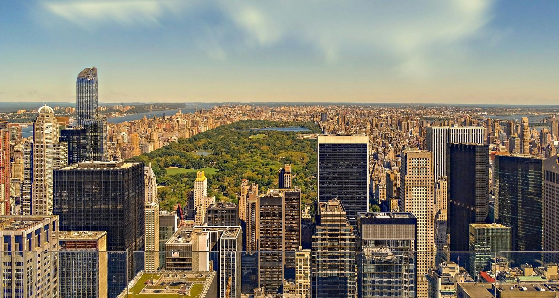 New York City skyline, Central Park, tall buildings, blue sky with some clouds.