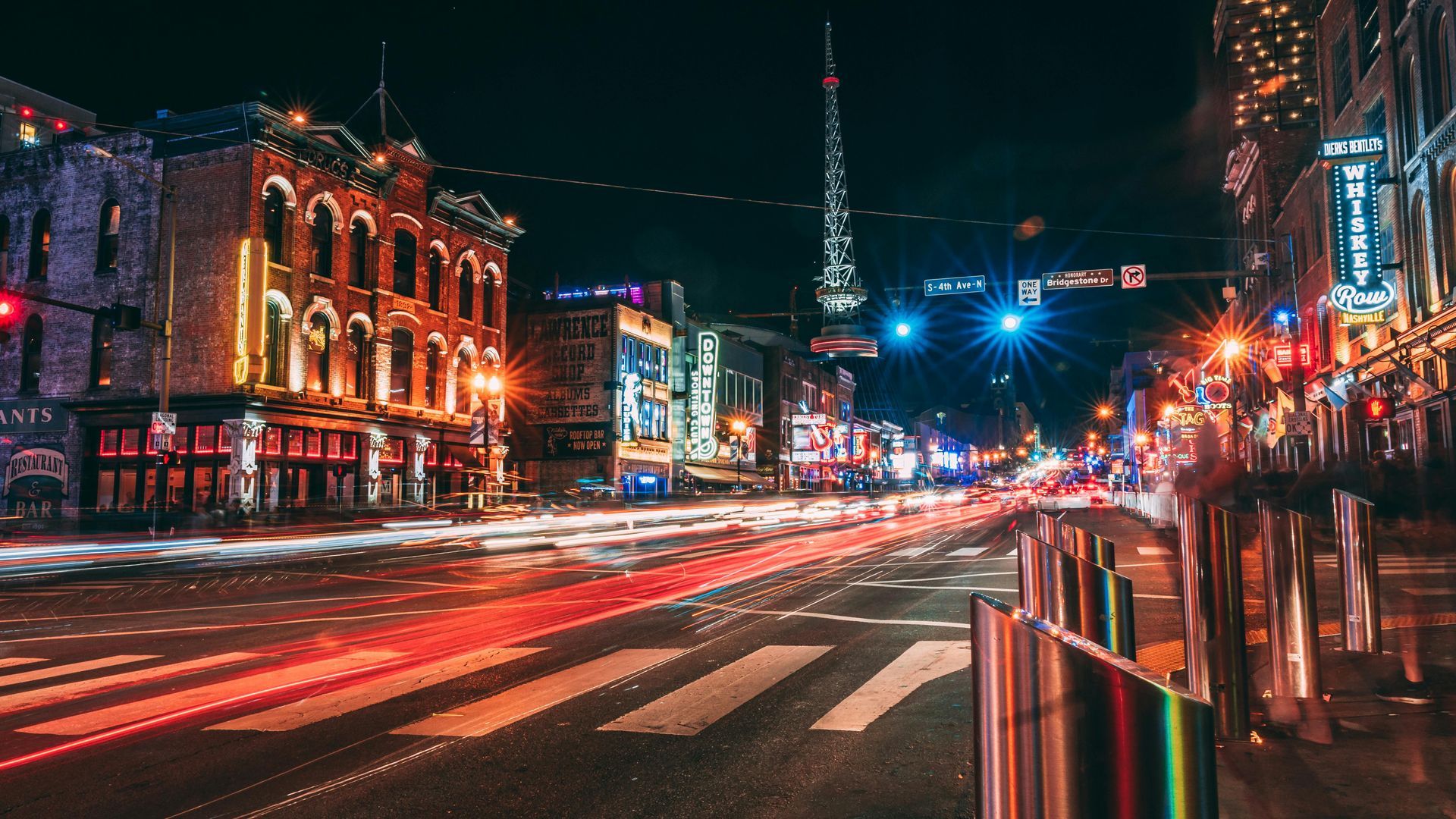 Nighttime street scene in Nashville, TN, with illuminated buildings, blurred car lights, and traffic lights.
