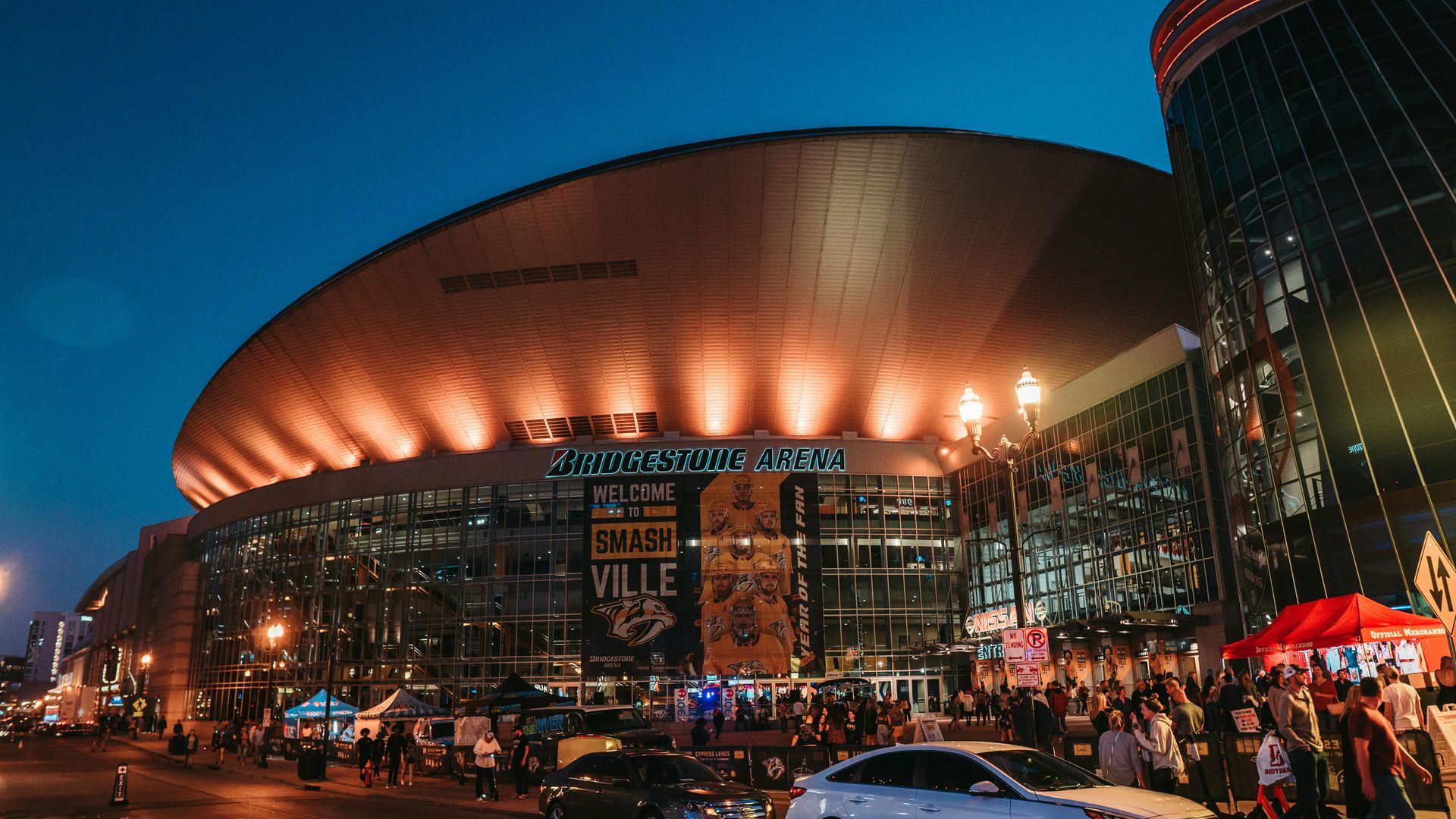 Night view of Bridgestone Arena, Nashville, with crowds, lights, and a banner advertising an event.