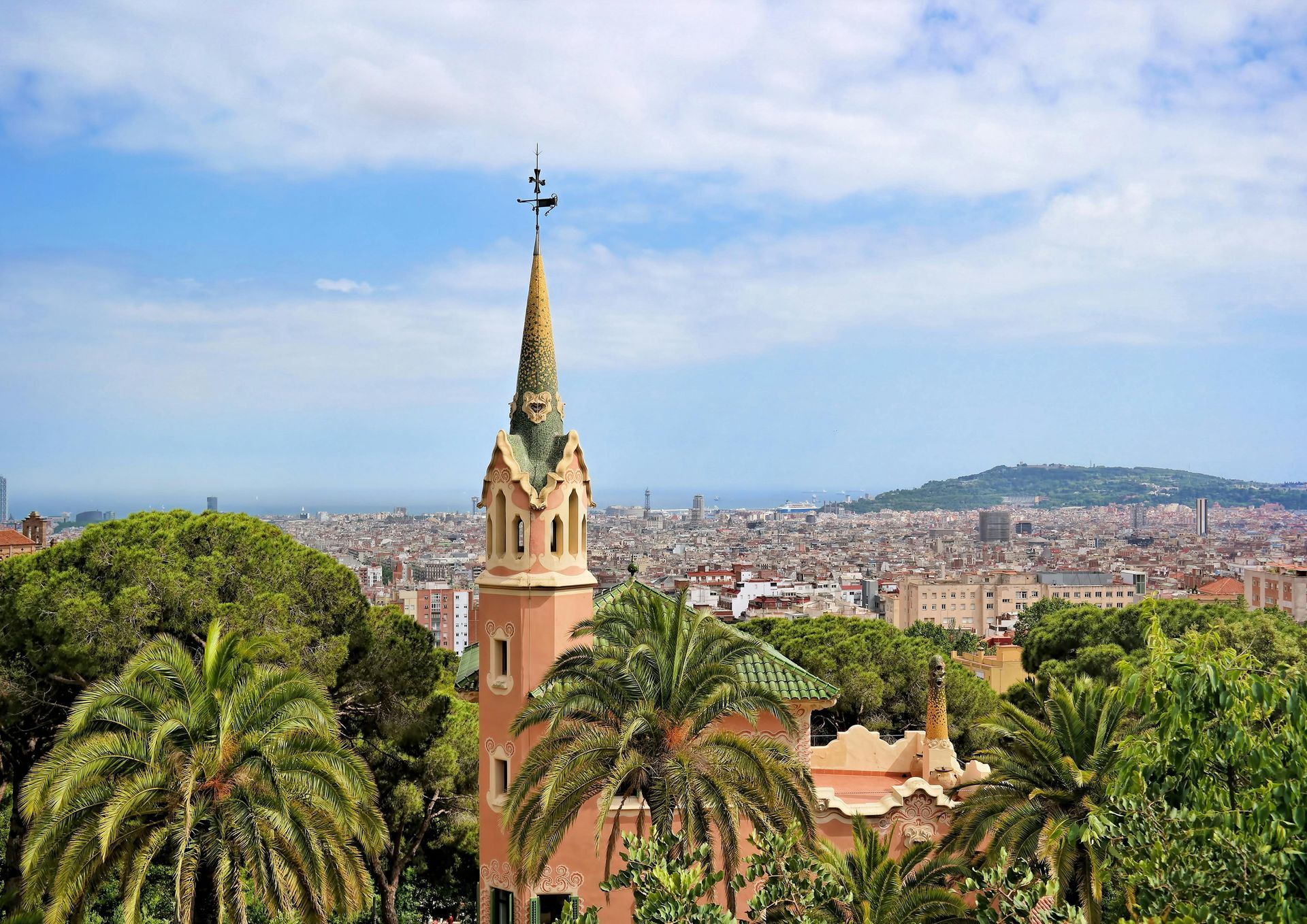 Tower in Park Güell, Barcelona, with city and sky views, surrounded by trees.