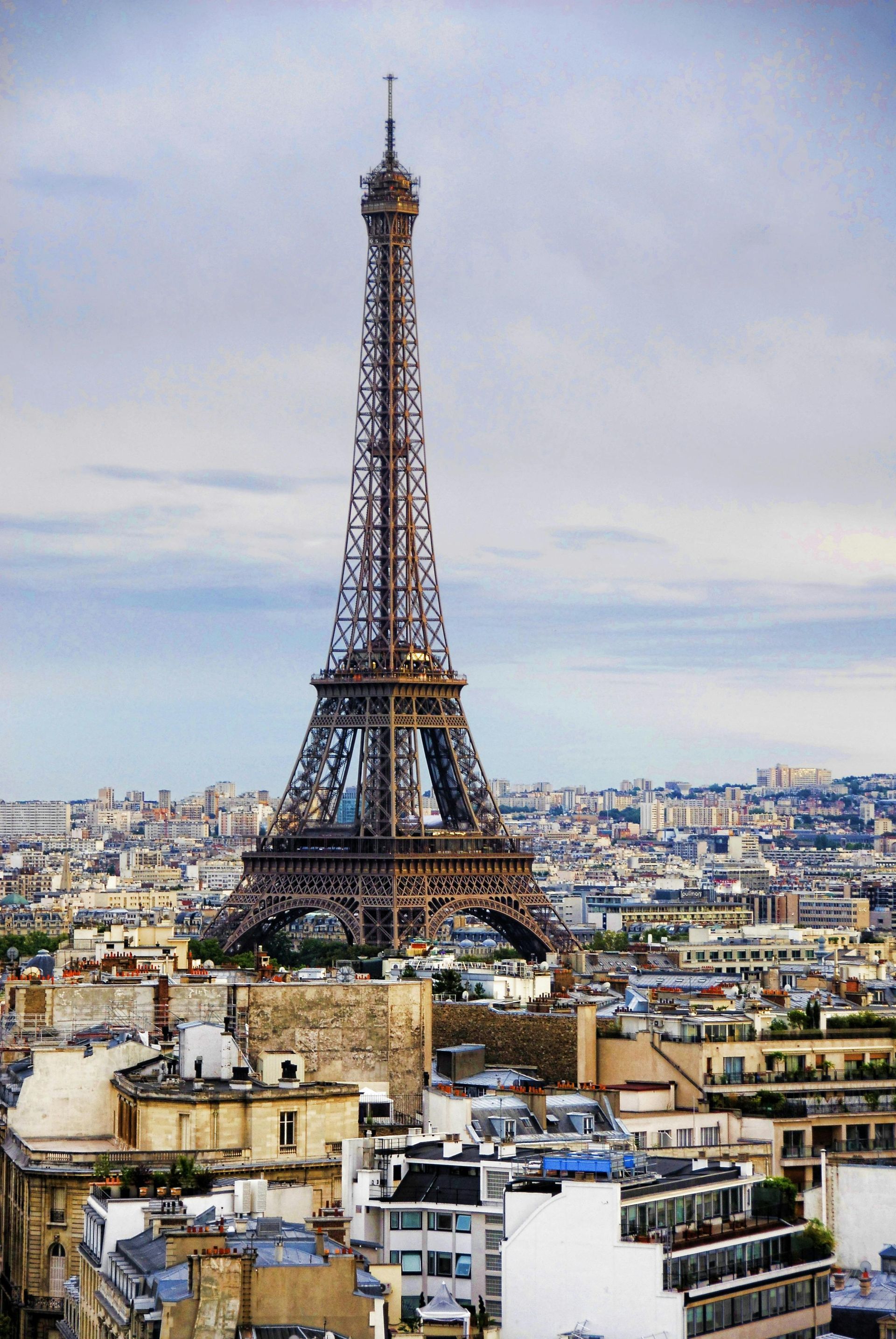 Eiffel Tower in Paris, France, towering over city rooftops against a cloudy sky.