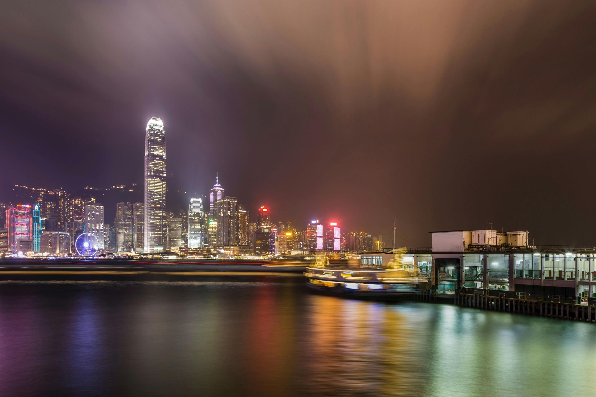 Night skyline of Hong Kong illuminated, with city lights reflecting in the water.