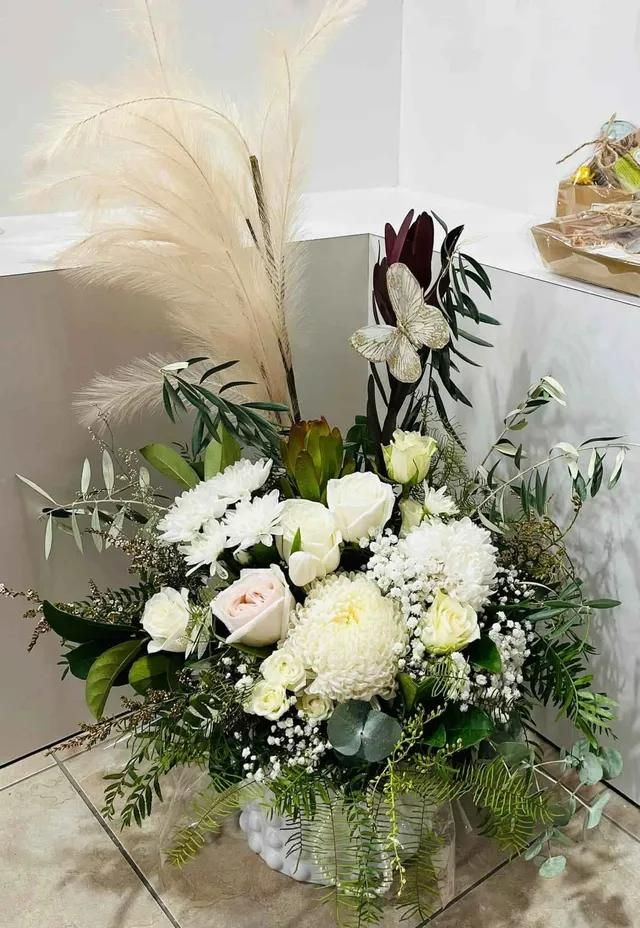 A Vase Filled With White Flowers and Greenery is Sitting on a Tiled Floor — Flower Hunt in Robina, QLD