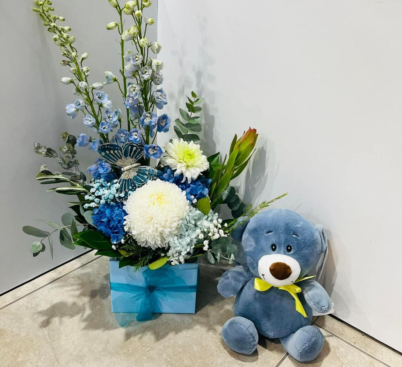 A Blue Teddy Bear is Sitting Next to a Vase of Flowers — Flower Hunt in Robina, QLD