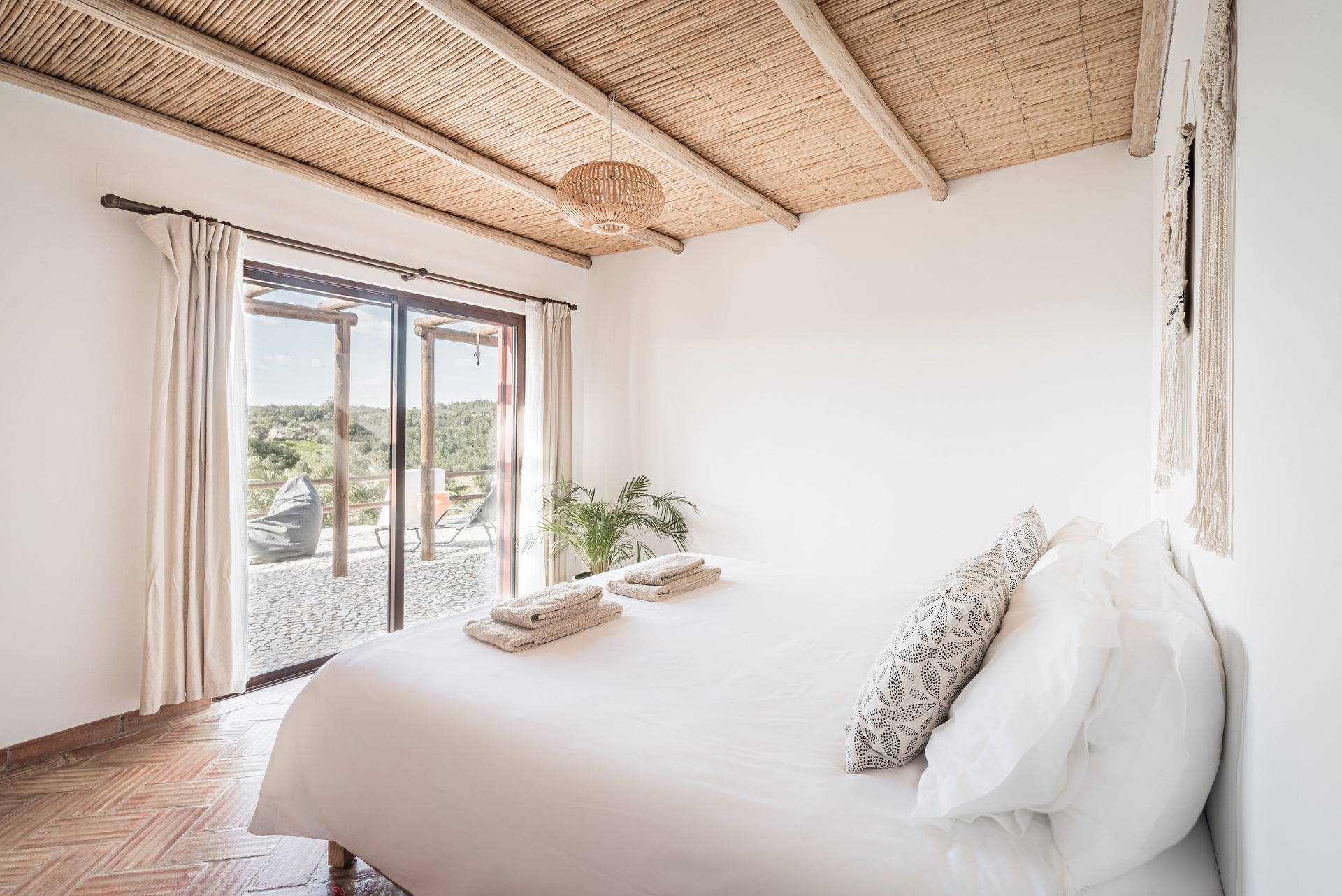 Bright bedroom with a white bed, sliding glass doors, and a woven ceiling with a view outside